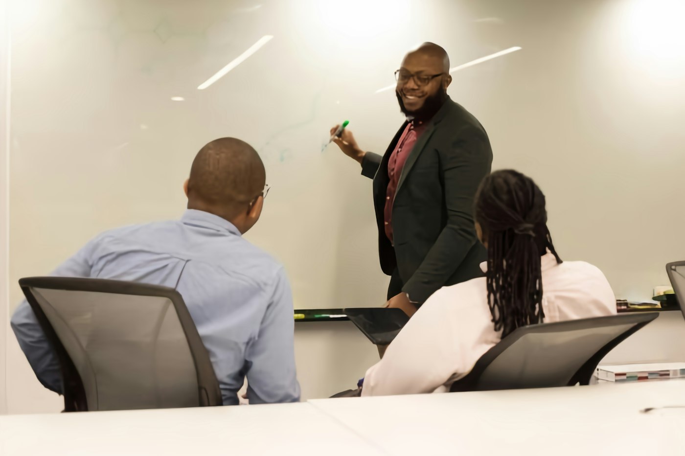 Consultant presenting at a whiteboard to two clients in a meeting room