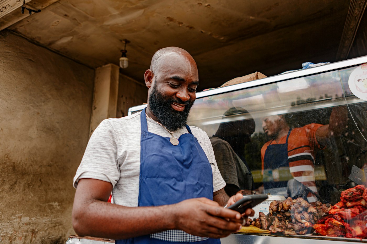Shopkeeper in an apron checking a payment on his phone behind the counter