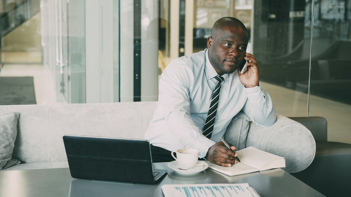 Procurement officer on the phone with a supplier, taking notes at his desk
